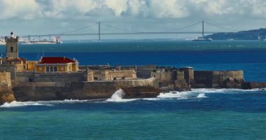 Arka planda ünlü bir köprü olan Portekiz 'deki bir kalenin insansız hava aracı görüntüsü. Portekiz, Carcavelos sahilinden deniz feneri kulesi olan Aziz Julian Kalesi. Carcavelos 'taki Atlantik okyanus dalgaları plajı.