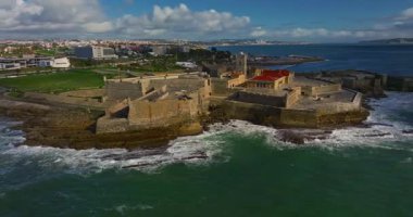 Arka planda ünlü bir köprü olan Portekiz 'deki bir kalenin insansız hava aracı görüntüsü. Portekiz, Carcavelos sahilinden deniz feneri kulesi olan Aziz Julian Kalesi. Carcavelos 'taki Atlantik okyanus dalgaları plajı.