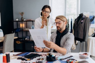 Şık giyinen olgun erkek ve kadından esinlenerek modern stüdyoda çalışırken çizimleri kağıt üzerinde tartışırlar. Moda endüstrisi ve yaratıcılık kavramı.