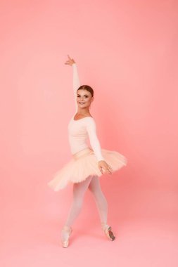 Esnek vücutlu mutlu genç bir kadın pembe stüdyo arka planında bale hareketleri yapıyor. Klasik dans, sanat ve favori hobi kavramı.