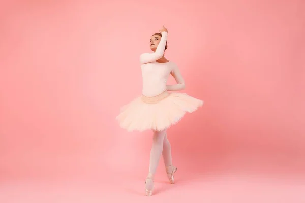ピンクのスタジオの背景の上の先端のつま先でバランスの取れたプロの衣装で熟練した白人のバレリーナ 公開若い女性は古典的なバレエ芸術の練習のために自由な時間を過ごす — ストック写真