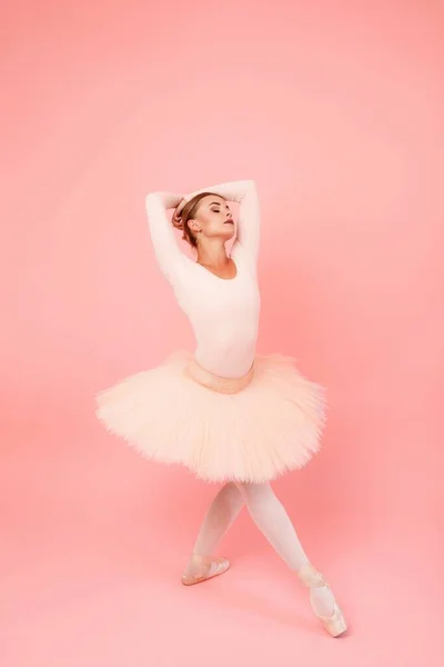 チュチュのエレガントな若い女性とスタジオでバレエダンスの動きを練習靴を指す 白人バレリーナとともに細い体運動以上ピンクの背景 — ストック写真