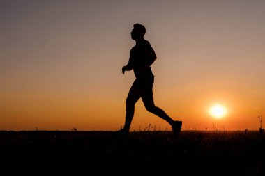 Güzel yaz günbatımında dışarıda koşan siluetli atletik genç adam. Kaslı vücudu olan beyaz bir adam akşam vaktini kardiyo egzersizleri için harcıyor..