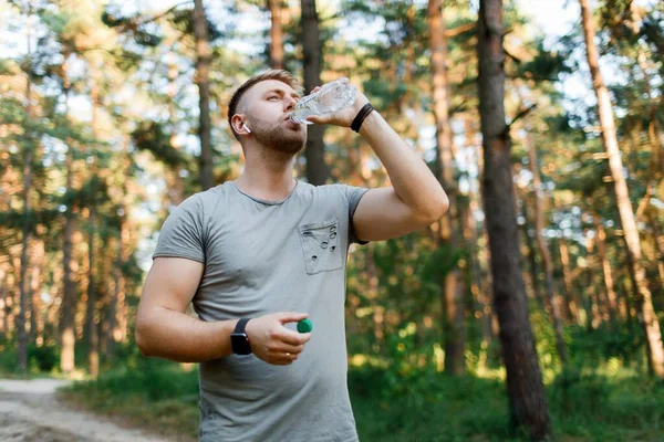 stock image Caucasian young guy in activewear drinking water from bottle after jogging at summer forest. Concept of people, healthy ande active lifestyles.