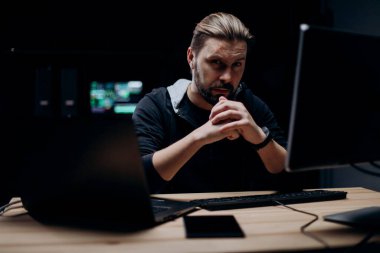 Modern bilgisayarlarla karanlık odada oturan zeki erkek hacker 'lar. Siyah kapüşonlu sakallı adam gece siber suçlar için kod yazıyor..