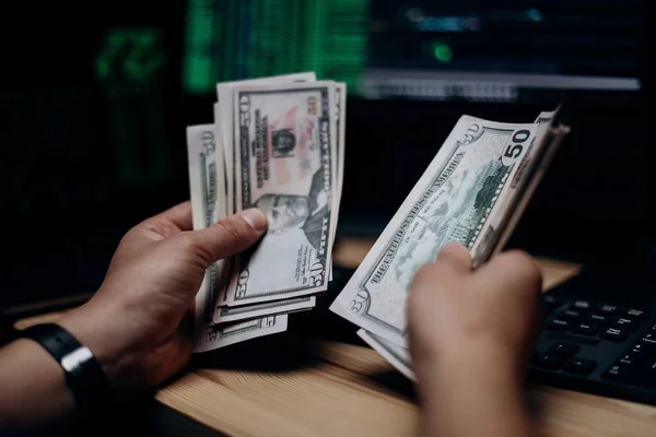 해커가 휴대용 컴퓨터를 가지고 어두운 달러화 지폐를 계산하는 마무리 짓습니다 — 스톡 사진