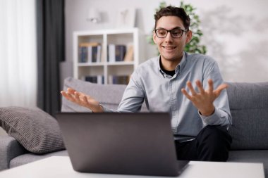 Gözlüklü ve sıradan giyinmiş yakışıklı beyaz adam dizüstü bilgisayar ekranına bakarken mutlu bir şekilde el kol hareketi yapıyor. İnsanlar ve modern teknoloji kavramı.