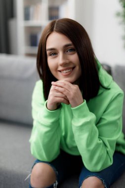 Kısa kahverengi saçlı hoş bir genç kadının portresi rahat koltukta boş vakit geçiriyor. Yeşil kapüşonlu ve kot giyen beyaz bir kadın..