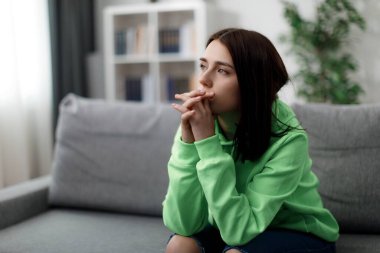 Kafkasyalı, sıradan giyinmiş, elleri çenesine yakın tutan ve koltukta otururken yan yan bakan bir kadın. Hayat sorunları ve endişeler kavramı.