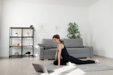 Spor giyim bölümünde beyaz bir kadın spor yaparken kablosuz bilgisayarda spor videosu izliyor. İnce vücutlu mutlu genç bir kadın vücut bakımına zaman ayırıyor..