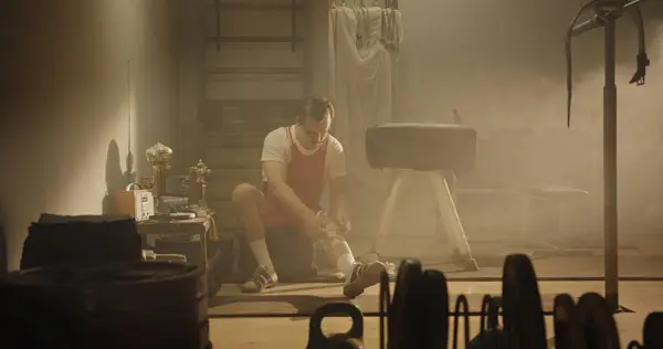 stock image In a hazy, vintage gym, a retro-styled weightlifter sits on a bench, preparing for competition. The atmosphere is filled with past glories, showcased by his awards and sports gear, capturing a