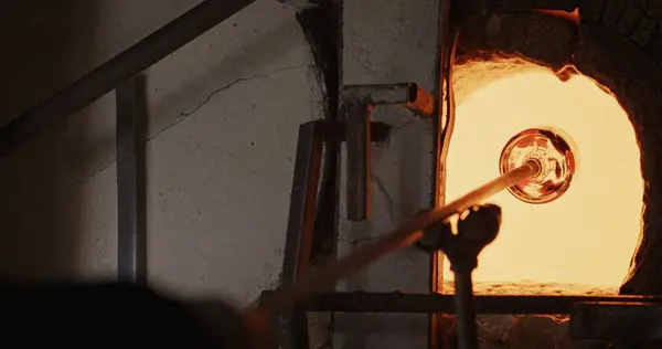 stock image A vivid scene in a glassblowing workshop where a glass artwork is heated inside a high-temperature furnace, showcasing the intense process of glass crafting.