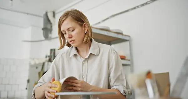 stock image A focused female ceramic artist carefully inspects a handcrafted dish in her bright, organized studio, ensuring top quality in her handmade creations. High quality 4k footage