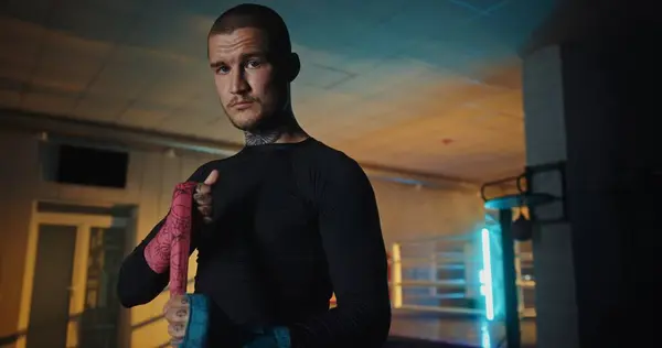 stock image Intense close-up of a determined young male boxer with distinctive tattoos, standing in a gym setting, mentally preparing before a vigorous training session.