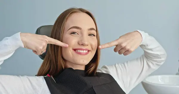 Stock image Showcasing a Flawless Smile: Young Woman Pointing at Her White Teeth in Dental Office. High quality 4k footage