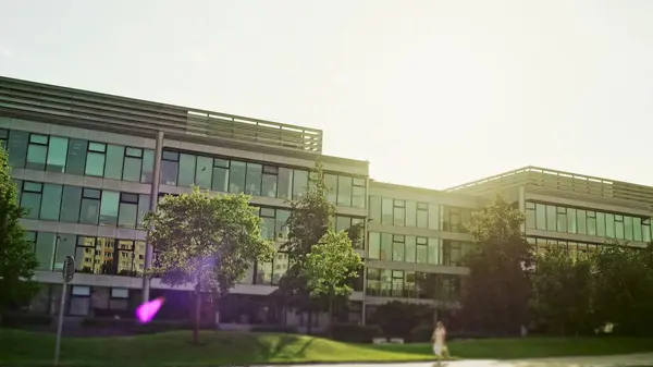 stock image A panning shot from right to left across the front facade of a modern glass office complex with colorful sun flare following the lens