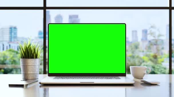 オフィスの机の上に緑の画面が空のノートパソコン風に揺れる木々や背景の近代的なビジネス街 — ストック動画