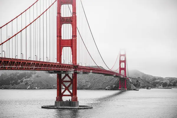 San Francisco 'daki Golden Gate Köprüsü sisli havada, kırmızı renkli siyah beyaz bir fotoğraf.