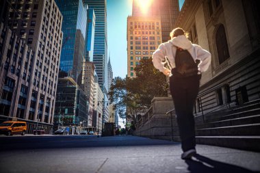Kaldırımda yürüyen bir kız, güneş ışınlarıyla aydınlatılmış New York 'un yüksek binalarını delip geçen.