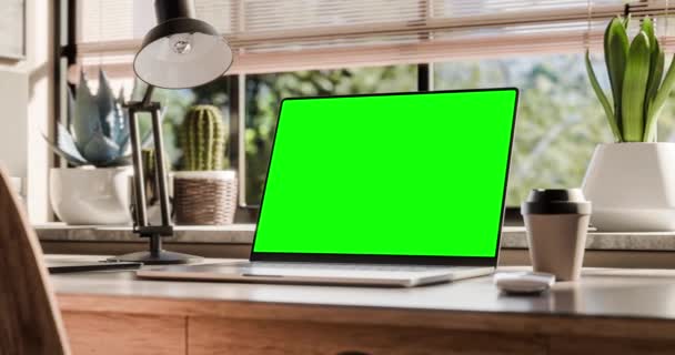 有一个空白屏幕的笔记本电脑放在阁楼式室内的时髦木制桌子上 背景上的绿色空间可以透过窗户看到 这台相机在计算机周围平稳地移动 — 图库视频影像
