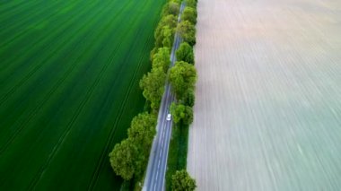 Tarlalardan yol manzaralı, bir tarafı yemyeşil, diğer tarafı ekime hazır. İnsansız hava aracı görüntüsü kırsal alanı yakalıyor.