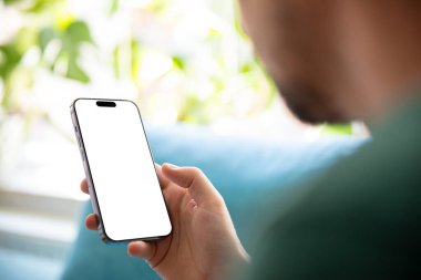 Elinde boş ekranlı akıllı bir telefon tutan parlak, yeşil bir çevrede koltukta dinlenen biri. Mobil uygulamaları, kullanıcı arayüzlerini veya dizayn şablonlarını sunmak için mükemmel resim.