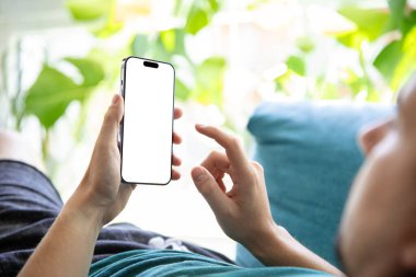 Elinde boş ekranlı akıllı bir telefon tutan parlak, yeşil bir çevrede koltukta dinlenen biri. Mobil uygulamaları, kullanıcı arayüzlerini veya dizayn şablonlarını sunmak için mükemmel resim.