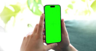 Yeşil ekranlı akıllı telefon tutan bir adam, açık yeşil bir ortamda bir kanepede dinleniyor. Mobil uygulamaları, kullanıcı arayüzlerini veya dizayn şablonlarını sunmak için mükemmel resim.