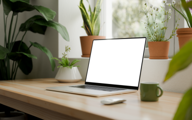 Boş şeffaf ekranlı bir dizüstü bilgisayar, parlak ve modern bir iç mekanda ahşap bir masanın üzerine yerleştirilmiş. Arka planda saksı bitkileri, doğal ışıklandırma ve minimalist stil.