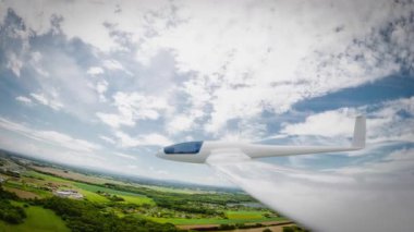 Pürüzsüz, beyaz bir planör zarif bir şekilde süzülüyor canlı bir gökyüzünün altındaki manzaranın üzerinde..