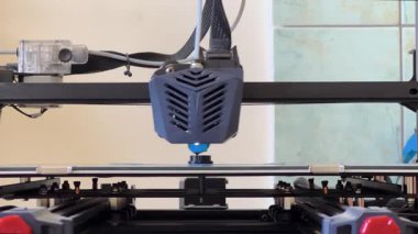 3D yazıcı başlığı mavi kabloyu çıkartıyor, baskı yatağının üzerine katman katman küçük bir nesne oluşturuyor.