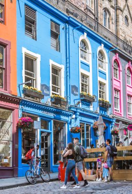 İskoçya, Edinburg - 24 Ağustos 2022: Victoria sokağı güzel bir kavis ve renkli dükkan cepheleriyle 1860 'da inşa edilmiş ve modaya uygun İskoç Baronluk tarzında tasarlanmıştır. İnsanlar yolda yürüyor.