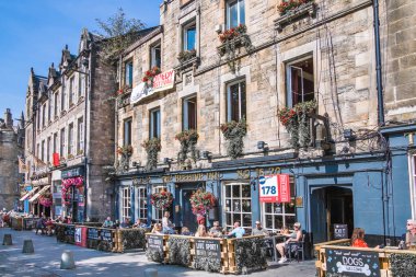 İskoçya, Edinburg - 24 Ağustos 2022: Victoria sokağı güzel bir kavis ve renkli dükkan cepheleriyle 1860 'da inşa edilmiş ve modaya uygun İskoç Baronluk tarzında tasarlanmıştır. İnsanlar yolda yürüyor.