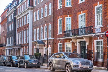 Londra, İngiltere - 9 Eylül 2023: Mayfair 'deki güzel periyodik binalar ve yolda park edilmiş lüks arabalar. Mayfair, lüks bir yaşam tarzıyla yaşamak için en zengin yerlerden biri.