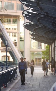 Londra, İngiltere - 30 Temmuz 2024: Güzel Canary Wharf ofis binaları gün batımında ve rıhtımda yürüyen insanlar