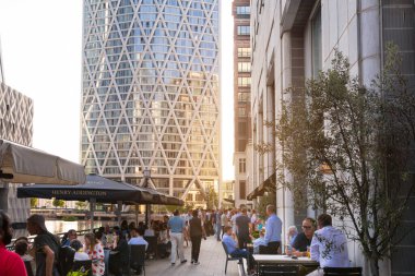Londra, İngiltere - 30 Temmuz 2024: Güzel Canary Wharf ofis binaları gün batımında ve rıhtımda yürüyen insanlar