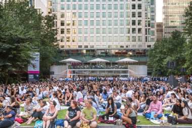 Londra, İngiltere - 30 Temmuz 2024: Canary Wharf 'taki bir çalışma gününden sonra insanlar rahatlıyor ve yayın izliyorlar. Gün batımında şehir merkezinde iş ve bankacılık