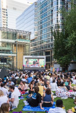 Londra, İngiltere - 30 Temmuz 2024: Canary Wharf 'taki bir çalışma gününden sonra insanlar rahatlıyor ve yayın izliyorlar. Gün batımında şehir merkezinde iş ve bankacılık