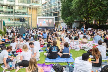Londra, İngiltere - 30 Temmuz 2024: Canary Wharf 'taki bir çalışma gününden sonra insanlar rahatlıyor ve yayın izliyorlar. Gün batımında şehir merkezinde iş ve bankacılık