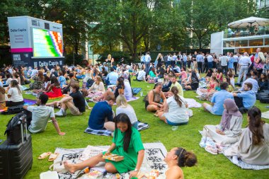 Londra, İngiltere - 30 Temmuz 2024: Canary Wharf 'taki bir çalışma gününden sonra insanlar rahatlıyor ve yayın izliyorlar. Gün batımında şehir merkezinde iş ve bankacılık