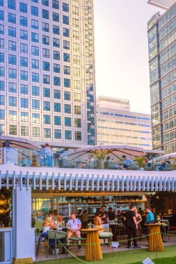 Londra, İngiltere - 14 Haziran 2025: İnsanlar Canary Wharf 'ta uzun bir çalışma gününden sonra içki içiyorlar. Gün batımında Kanada meydanında bar.
