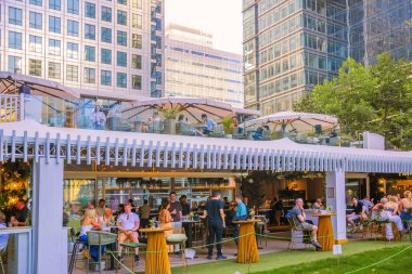 Londra, İngiltere - 14 Haziran 2025: İnsanlar Canary Wharf 'ta uzun bir çalışma gününden sonra içki içiyorlar. Gün batımında Kanada meydanında bar.