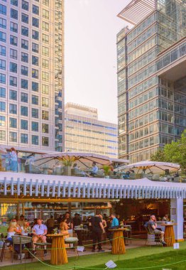 Londra, İngiltere - 14 Haziran 2025: İnsanlar Canary Wharf 'ta uzun bir çalışma gününden sonra içki içiyorlar. Gün batımında Kanada meydanında bar.