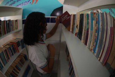 Tanhacu, Bahia, Brezilya - 31 Mayıs 2025: Bir okul kütüphanesinde devlet okulundan genç bir öğrenci, kitaplarını düzenliyor veya seçiyor..