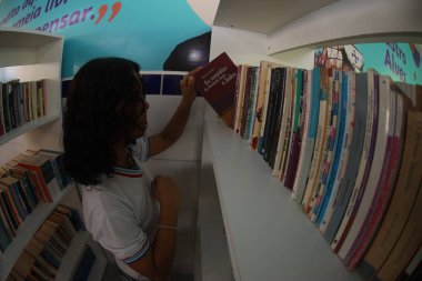 Tanhacu, Bahia, Brezilya - 31 Mayıs 2025: Bir okul kütüphanesinde devlet okulundan genç bir öğrenci, kitaplarını düzenliyor veya seçiyor..