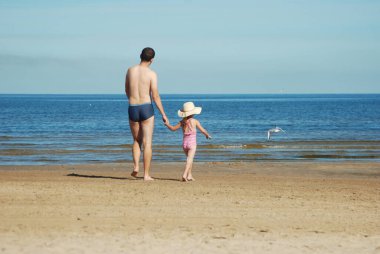 Kızımla babam yaz kumsalında denize doğru yürüyorlar..