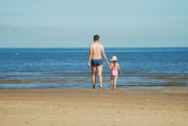 Kızımla babam yaz kumsalında denize doğru yürüyorlar..