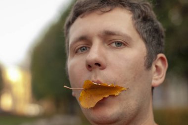 Dişlerinde sonbahar yaprağı olan genç bir adamın portresi..