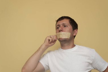 Genç bir adam ağız bandajını çıkarmaya çalışıyor. Konuşma özgürlüğü kavramı, konuşma, konuşma, özgür ol..