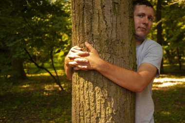 Genç adam parkta bir ağaca sarılıyor. Danimarkalı ve Norveçli Hygge kavramı, rahat bir ortam ve rahatlık, doğa ve insanlar, çevre dostu.